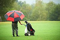 Man with colorist umbrella and electric golf cart under rain in the golf course.