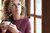 Serene people concept lifestyle. One woman drinking coffee or healthy beverage tea alone ner the window at home looking outside and thinking. Dreamerf...