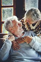 Happy senior couple hug and enjoy time together at home sitting on che chair and smiling each other. Concept of old people mature relationship. Joy re...