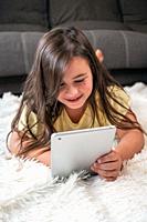 Adorable little girl using a digital tablet on the floor at home. High quality photography.