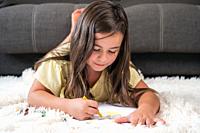 Cheerful little girl lying on the floor drawing . High quality photography.