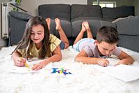 Siblings playing together at home. little boy and girl lying on the carpet and drawing on white sheets of paper with colorful crayons. High quality ph...