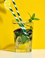 Transparent glass with lemonade, mint leaves, lemon slices and blackberries in the middle.