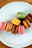 Colored macaroons on white plate on wooden board.