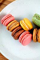 Colored macaroons on white plate on wooden board.