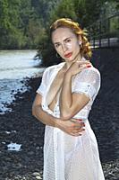 attractive young woman, in transparent garment, self-confident, on rocky river bank.