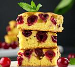 Baked pieces of sponge cake with red ripe cherries on a white wooden board.