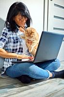 Mature Woman searching vet website on laptop to register cat for veterinary consultation, Freelancer female typing on laptop sitting on the floor at h...