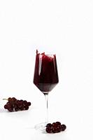 Wine glass with a splash of red wine and grapes isolated on white background copy space luxury.