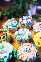 Various cupcakes decorated with colorful flower icing on wooden table, floral bouquet, wedding cake, High tea, Holiday concept Mothers day.