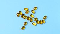 Yellow capsules with fish oil on a blue background, top view.