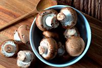 White bowl with portobello mushrooms on wooden board.