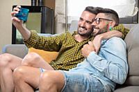 Young smiling gay couple taking selfie at home. High quality photography.