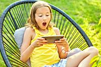 Happy kid girl playing game on mobile phone in the park outdoor, child using smartphone at home garden, backyard, sunlight, smartphone addiction.