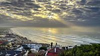 Sun rises over the sea and village of Muizenberg beach and Surfer's Corner.