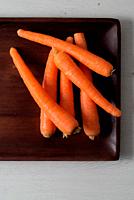Raw carrots on a wooden tray.