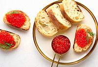 Sandwiches with red caviar and bread in a round plate on a white table, top view.