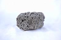 Unpolished black pumice rock cutout. Isolated over white fabric cloth.