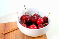 White bowl with fresh cherries on wooden board.