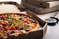 Large Pizza in open carton box and cutter on kitchen table closeup view.