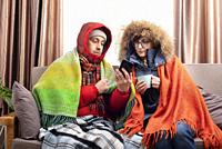 Middle age family in parkas drinking coffee on the sofa while using smartphone in their cold living room.