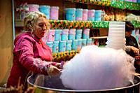 Whisked sugar dreams into reality: A skilled woman spins magic at a street stall, crafting the sweet allure of cotton candy under the urban glow.