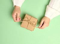 Female hands holding a gift box on a green background. View from above.