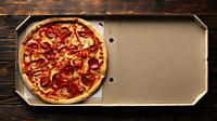 Pepperoni pizza with bell peppers in open carton box on dark wooden table flat lay with copy-space.