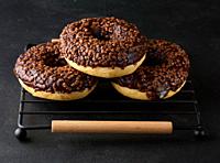 Chocolate donuts sprinkled with crushed nuts on a black table.