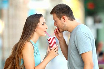 Side view portrait of a happy couple sharing a takeaway refreshment in the street-stock-photo