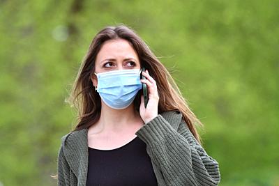 Topic image Corona: A young woman with protective mask, face mask, community mask is on the phone on April 24th, 2020. | usage worldwide. - Munich/Bayern/Deutschland-stock-photo