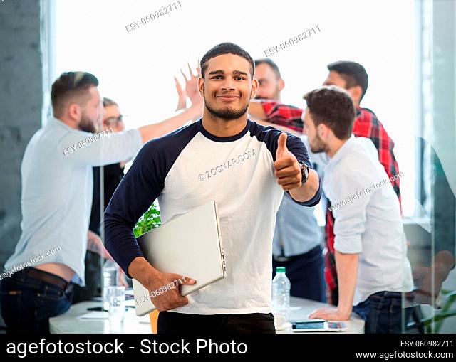 Image of handsome businessman showing thumb-up sign in office interior. Happy man smiling for camera and holding clipboard