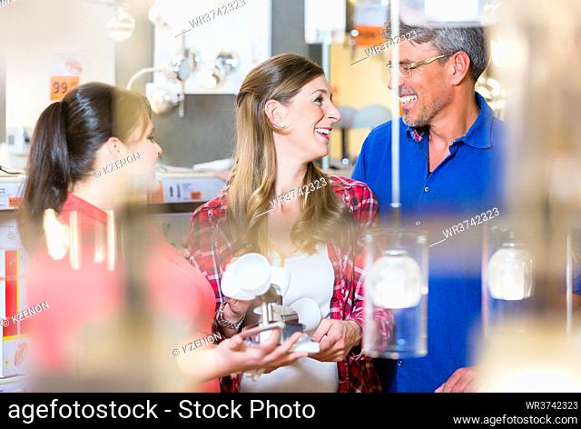 Clerk giving advice about lamps to couple, woman and man, in electrical goods department of hardware store