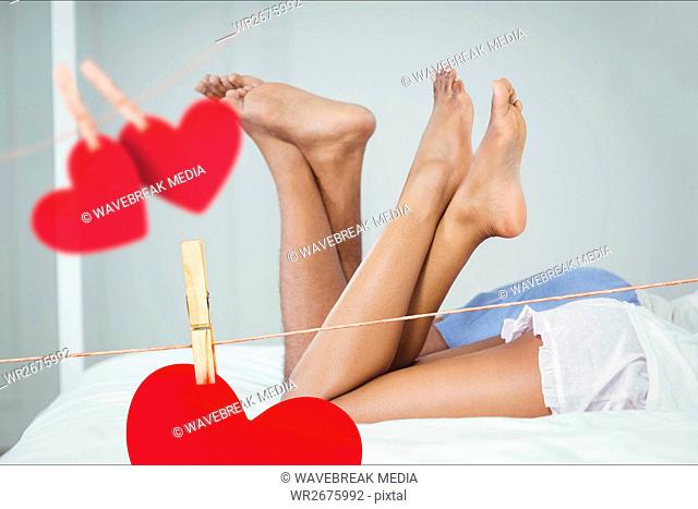 Composite image of red hanging hearts and couple lying on bed with crossed leg