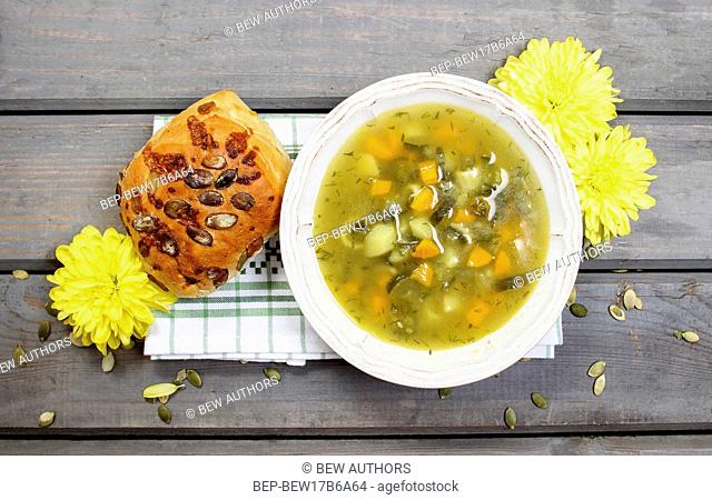 Vegetable soup on wooden table. Basket with fresh bread in the background