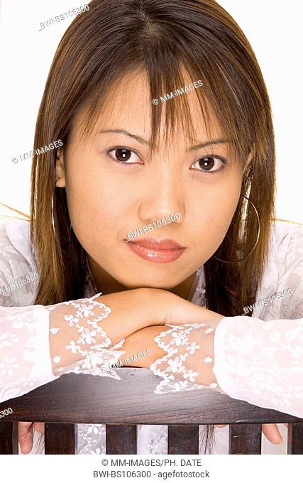 A pretty young asian girl rests her head and arms on a chair