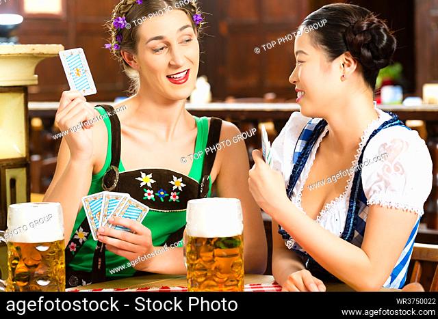 In Pub - friends in Tracht, Dirndl and Lederhosen drinking a fresh beer in Bavaria, Germany playing cards