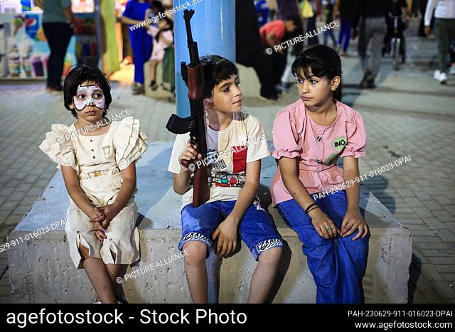29 June 2023, Iraq, Baghdad: A child sits with a toy gun at Al-Zawraa amusement park, during the celebrations of Eid al-Adha holiday in Baghdad