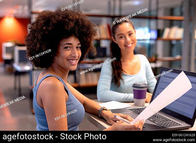 Portrait of smiling biracial businesswoman with hispanic female colleague working together in office