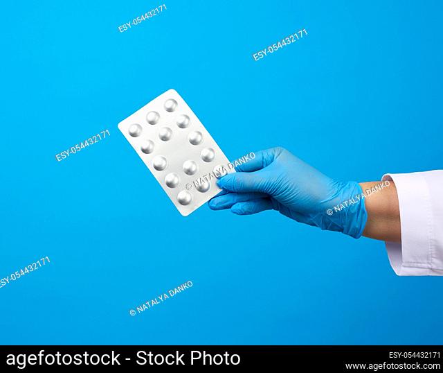 female hand with blue sterile gloves holds a pills in a blister, concept for drug treatment of diseases, blue background