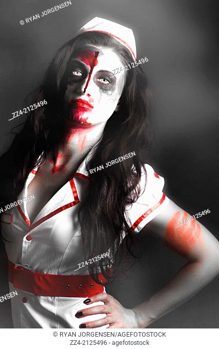 Foggy horror scene of a scary zombie nurse posing in the shadow of darkness with facial wounds and a bloody mouth