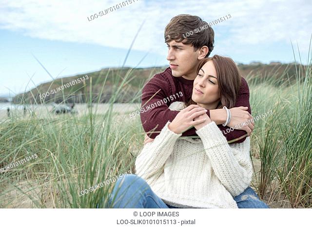 A young couple cuddling in the dunes on the beach at Porthmadog