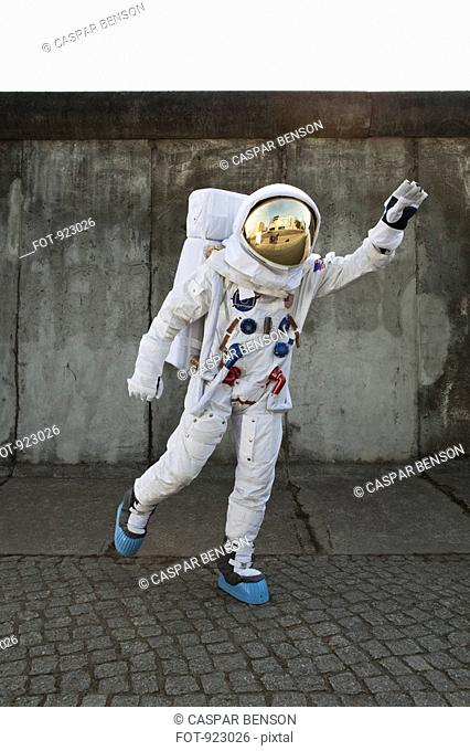 An astronaut on a city sidewalk pretending to take off in flight