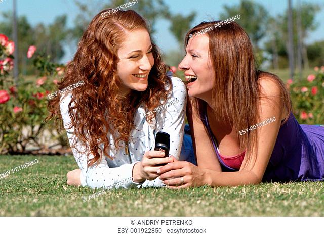 Two girlfriends in park with a mobile phone