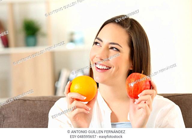 Happy woman wondering about an apple and orange sitting on a couch in the living room at home