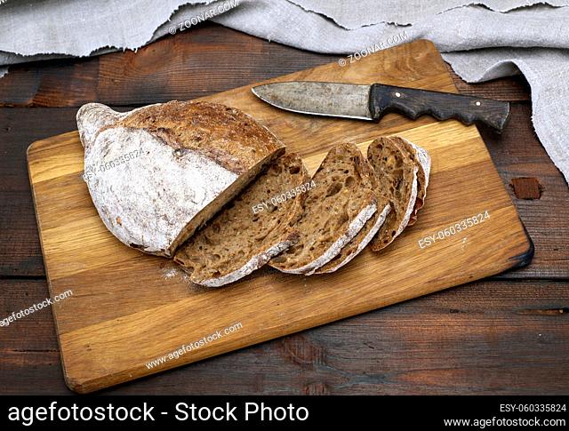 sliced bread with rye flour flour on a brown wooden board, top view