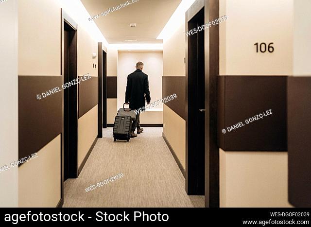 Businessman walking with briefcase and luggage at hotel corridor