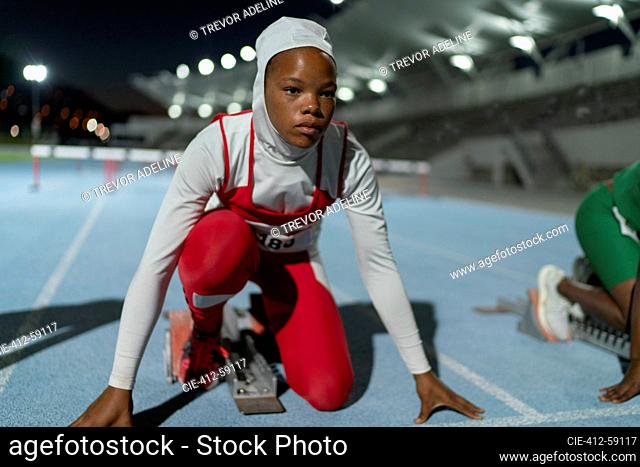 Focused female track and field athlete in hijab at starting block