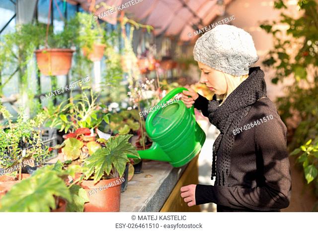 Portrait of florists woman working with flowers in a greenhouse holding a watering can in her hand. Small business owner