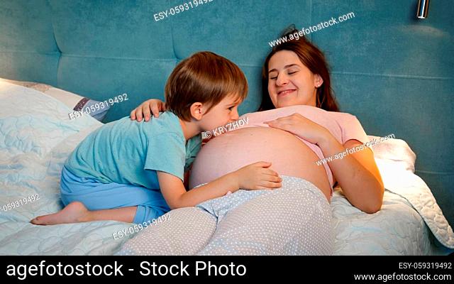 Young pregnant mother with big belly lying with hr older son in bed at night. Family having good time together and expecting baby